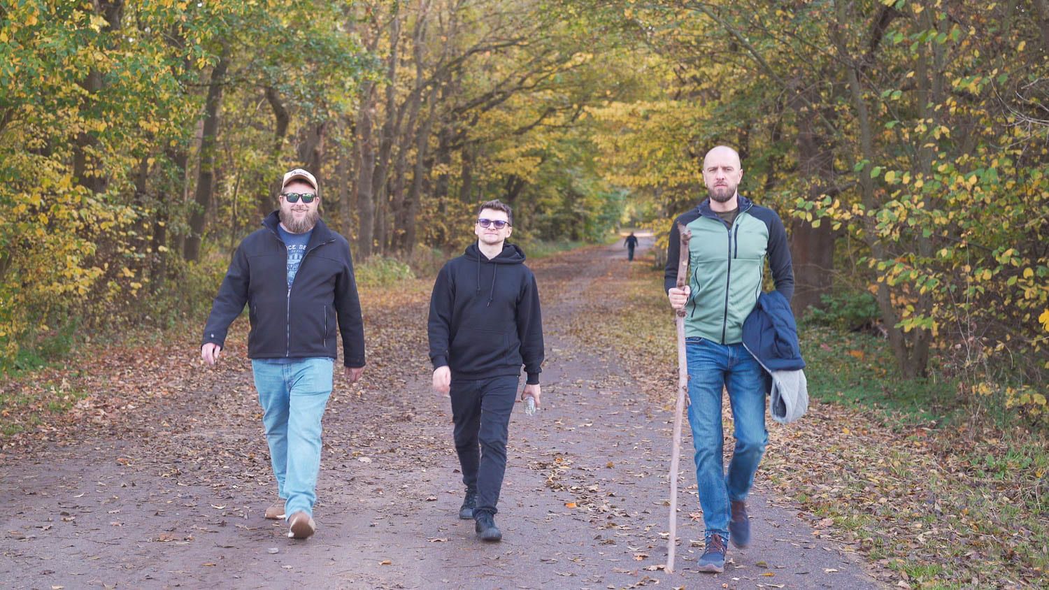 Three men walking on a leaf-covered path with autumn trees