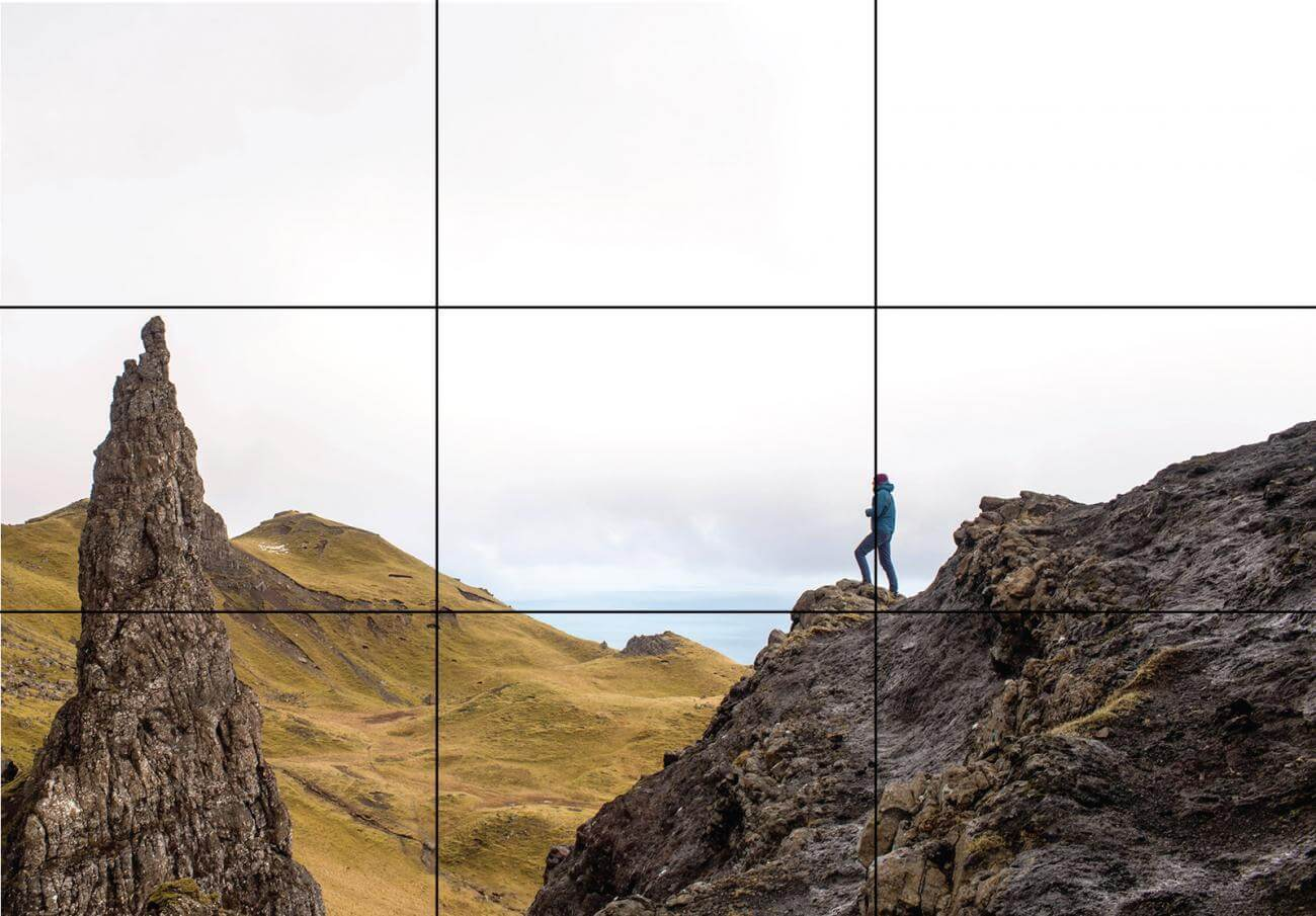 Person standing on a rocky cliff with grid overlay for composition.