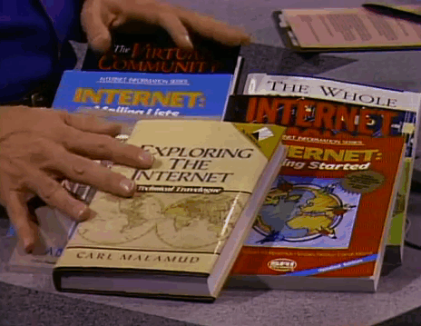 Hands flipping through a book titled 'Exploring The Internet' among other books